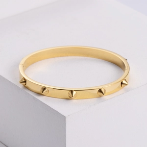 Elegant gold titanium steel nail bracelet with cone rivets on a geometric stand