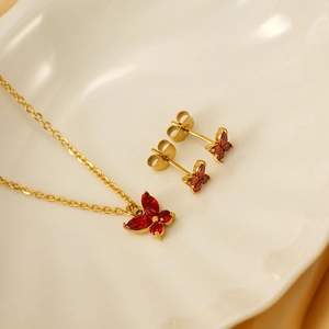 Goldenes Schmetterling-Schmuckset mit roten Steinen auf einer Keramikschale