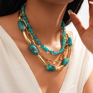 Detail of layered bohemian necklace with gold accents and teal acrylic beads on model
