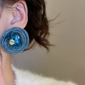 Detail of blue flower earrings with colorful gems on model showing weaving texture