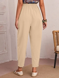 Detail view of beige linen-blend trousers featuring elastic waist and natural fabric texture