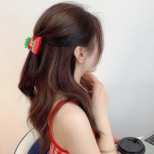 Detail view of a cute red strawberry hair claw clip worn on a casual hairstyle