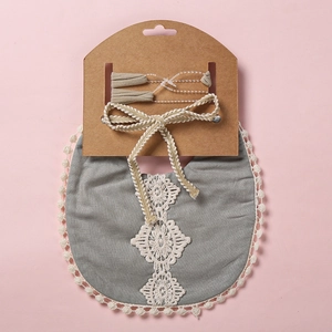 Détail d'un bavoir bébé avec dentelle au crochet et pompons crème sur tissu en coton gris