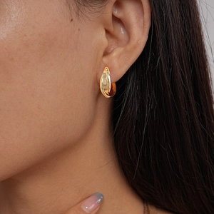 Detail of model wearing gold layered intertwining metal clip-on earrings with high polish