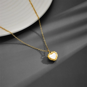 Macro detail of heart-shaped white shell pendant with vintage golden engraved border