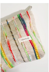 Gros plan d'une trousse à maquillage rayée avec texture tissée et logo H&R BAG