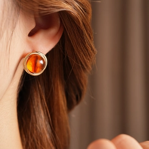 Close-up of amber resin stud earrings with gold metal frame worn by a female model