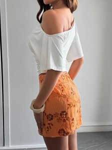 Detail of white off-shoulder top and orange beaded mini skirt with sequin embroidery