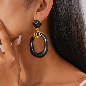 Close-up of oversized black resin earrings with golden metal accents on a model