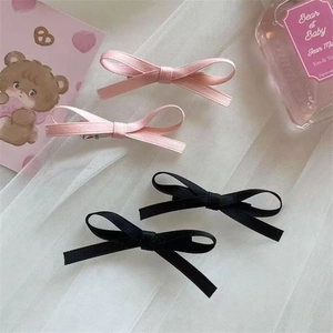 Close-up of pink and black satin ribbon bow hair clips on soft white mesh background