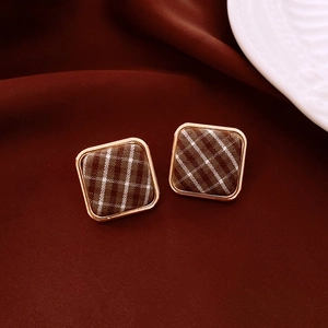 Détail de boucles d'oreilles carrées en tissu à carreaux marron avec bordure dorée
