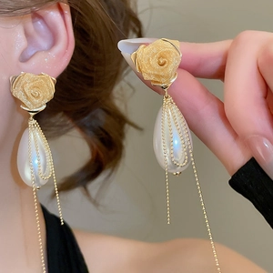 Detailed macro view of matte gold rose stud with large teardrop pearl and fringe