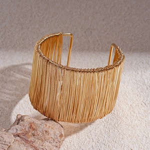 Macro shot of layered golden wire-wrapped cuff bracelet on beige stone textured surface