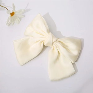 Detail of a creamy white satin bow hair clip featuring silky texture and elegant folds