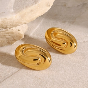 Detail of gold oval spiral earrings on a natural light stone background with soft shadows
