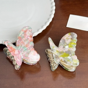 Elegant acetate butterfly hair claws in pink and yellow on a wooden desk setting