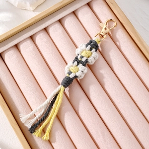 Handmade woven daisy flower keychain with tassels on pink velvet jewelry tray for bags
