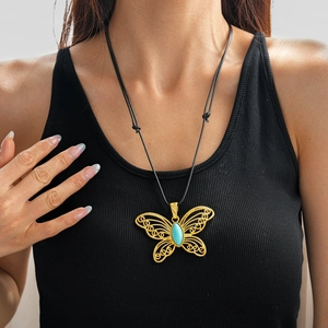 Detail of hollow gold butterfly pendant with turquoise stone on black wax cord