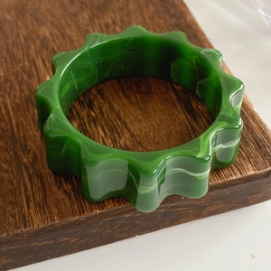 Macro detail of wave-shaped emerald green resin bangle with white marble textures on wood