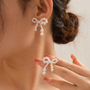 Close-up of pearl bow earrings with ribbon knot design on a person's ear