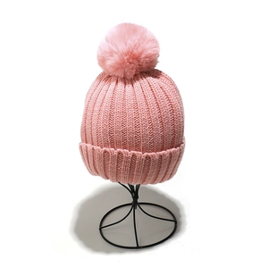 Pink knit beanie with faux fur pom-pom on stand, thick ribbed cuff for winter warmth