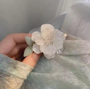Close-up of a white camellia hair clip with green leaves and pearlescent finish