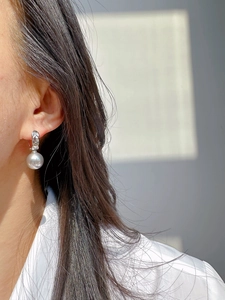 Close-up of a silver quilted U-shaped earring with a lustrous grey pearl on a model