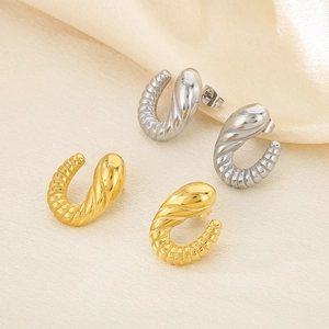 Detail view of gold and silver spiral horn earrings on beige silk fabric background