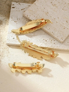 Detailed view of three vintage gold metal leaf hair clips on a textured stone surface