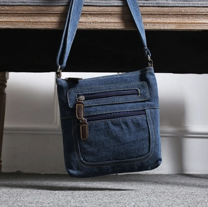 Close-up of denim shoulder bag featuring multi-zipper pockets and brown leather details