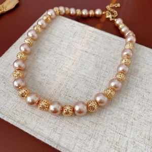 Detail of beaded necklace with gold hollow metal beads and pearls on linen