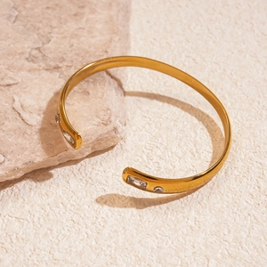 Close-up of golden stainless steel sun droplet bangle with white zircon inlays