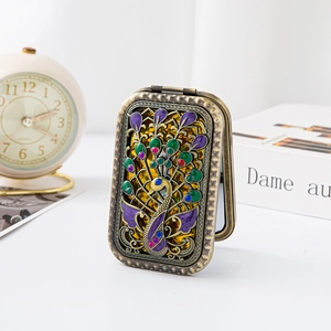 Detail of a vintage metal folding mirror with an ornate peacock relief and colorful enamel