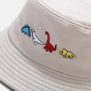 Foldable beige cotton bucket hat featuring colorful cartoon dinosaur embroidery details