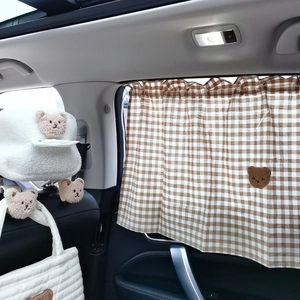 Close-up of brown plaid sunshade and white plush bear tissue holder in a car interior