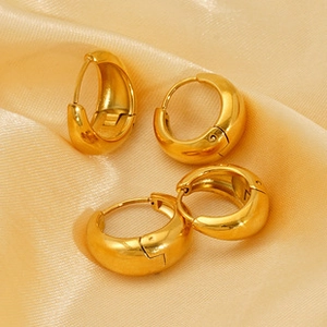 Close-up of golden round hoop earrings on soft peach silk fabric highlighting metal texture
