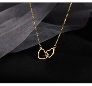 Detail of interlocking double heart pendant in gold finish on elegant mesh backdrop