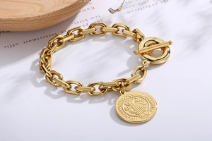 Close-up of a gold chunky chain bracelet with T-bar clasp and vintage coin pendant