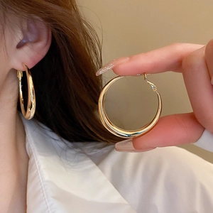 Large polished gold hoop earrings with thick tubular design worn by a female model