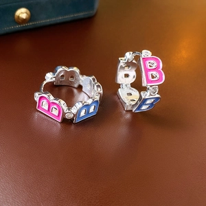 Macro detail of silver B-letter earrings with pink and blue enamel and zircon inlay
