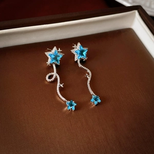 Macro detail of star-shaped blue zircon earrings with silver fringe tassels on leather
