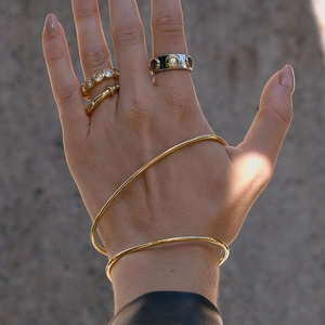 Close-up of minimalist gold bangles and stacked rings with white stones on a model's hand