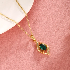 Detail showing an elegant gold eye-shaped pendant with a green gemstone on pink fabric