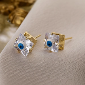 Macro detail of square zircon stud earrings with blue evil eye motif in gold plating