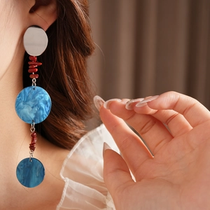 Close-up of asymmetric long tassel earrings featuring blue resin discs and red beads on a model