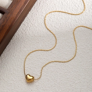 Collana cuore oro minimalista con pendente 3D lucido su uno sfondo bianco strutturato