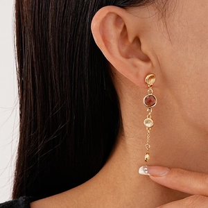 Close-up of gold dangle earrings with red glass beads worn by a female model