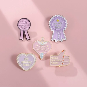 Detail of pink and purple enamel pins with Heart Breaker and No Drama Club text