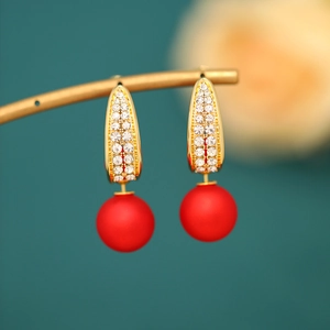 Macro detail of elegant gold earring with sparkling pavé stones and red matte pearl charm