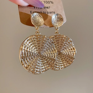 Detail view of gold circular earrings with delicate woven metal texture on brown card